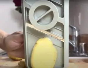 Slicing potato with adjustable mandoline slicer in kitchen setting. Kitchen tool for precise vegetable cuts.